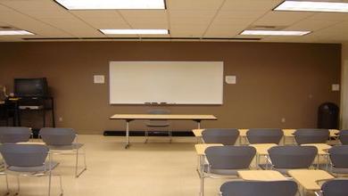 The whiteboard, seated desks, television, tables and projection equipment of LLC 133.