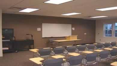 The whiteboard, seated desks, television, tables and projection equipment of LLC 144.